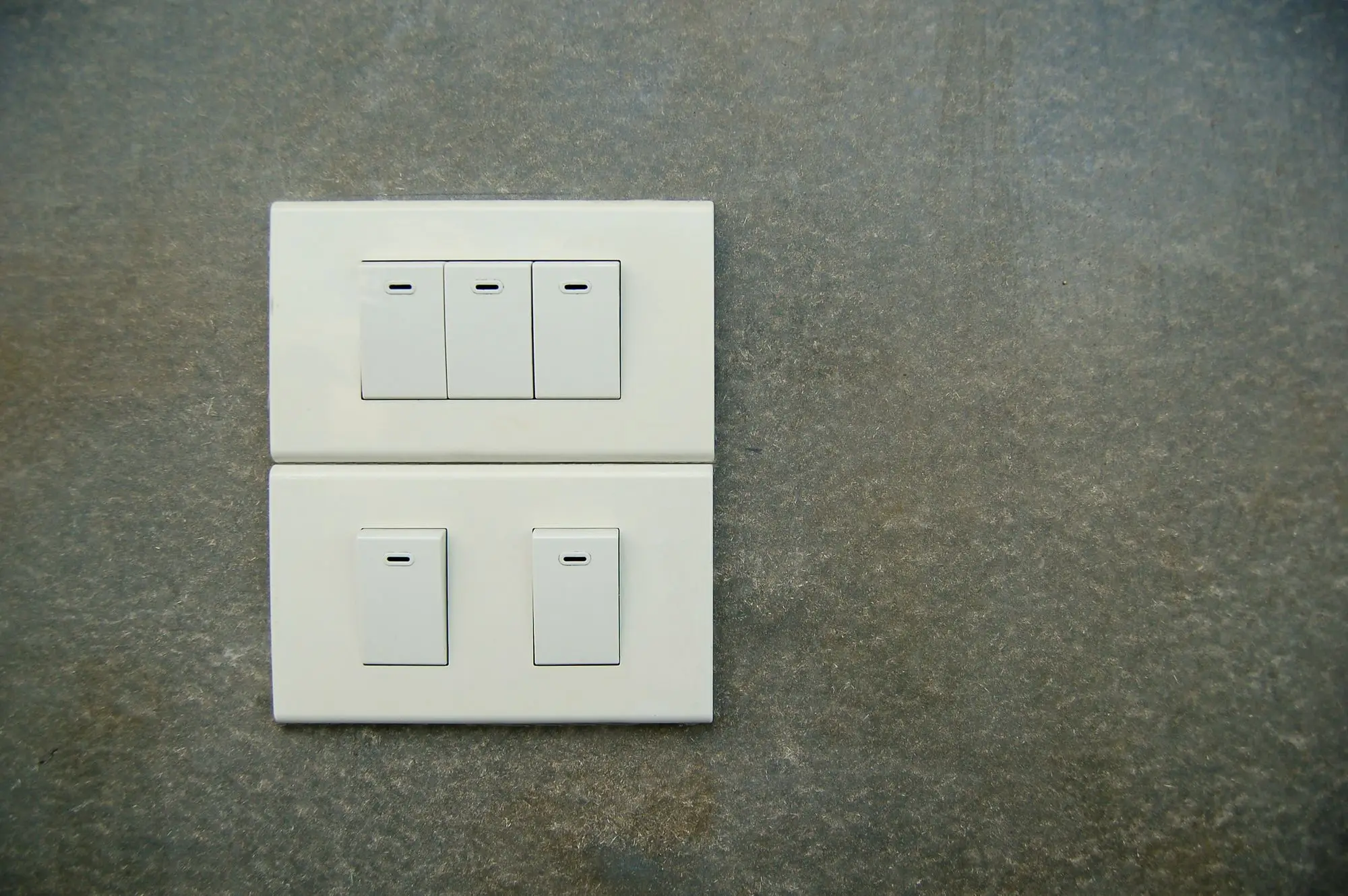 Two white rocker light switches on a pale textured stone wall