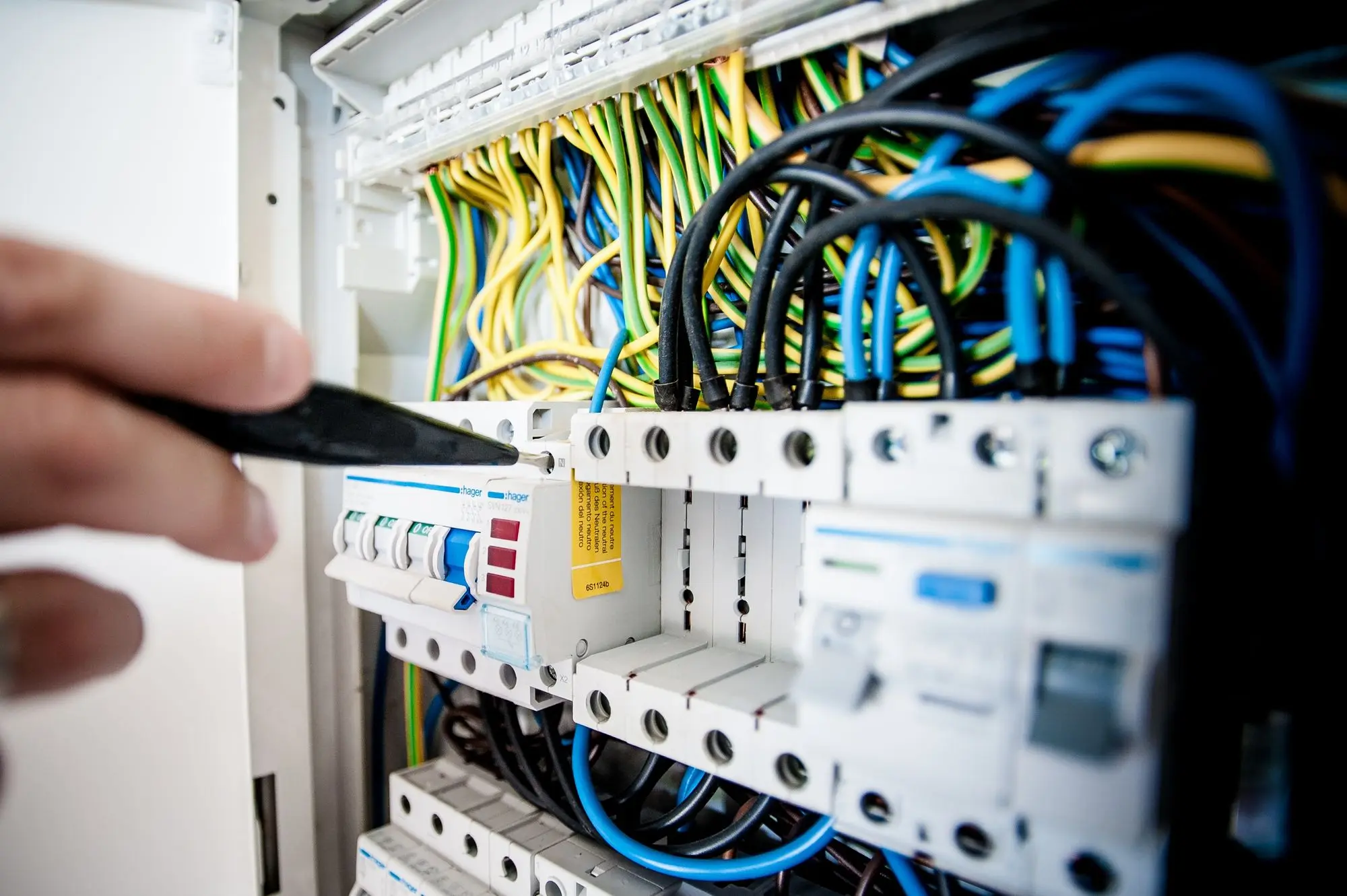 A hand working inside a breaker panel among coloured conductors