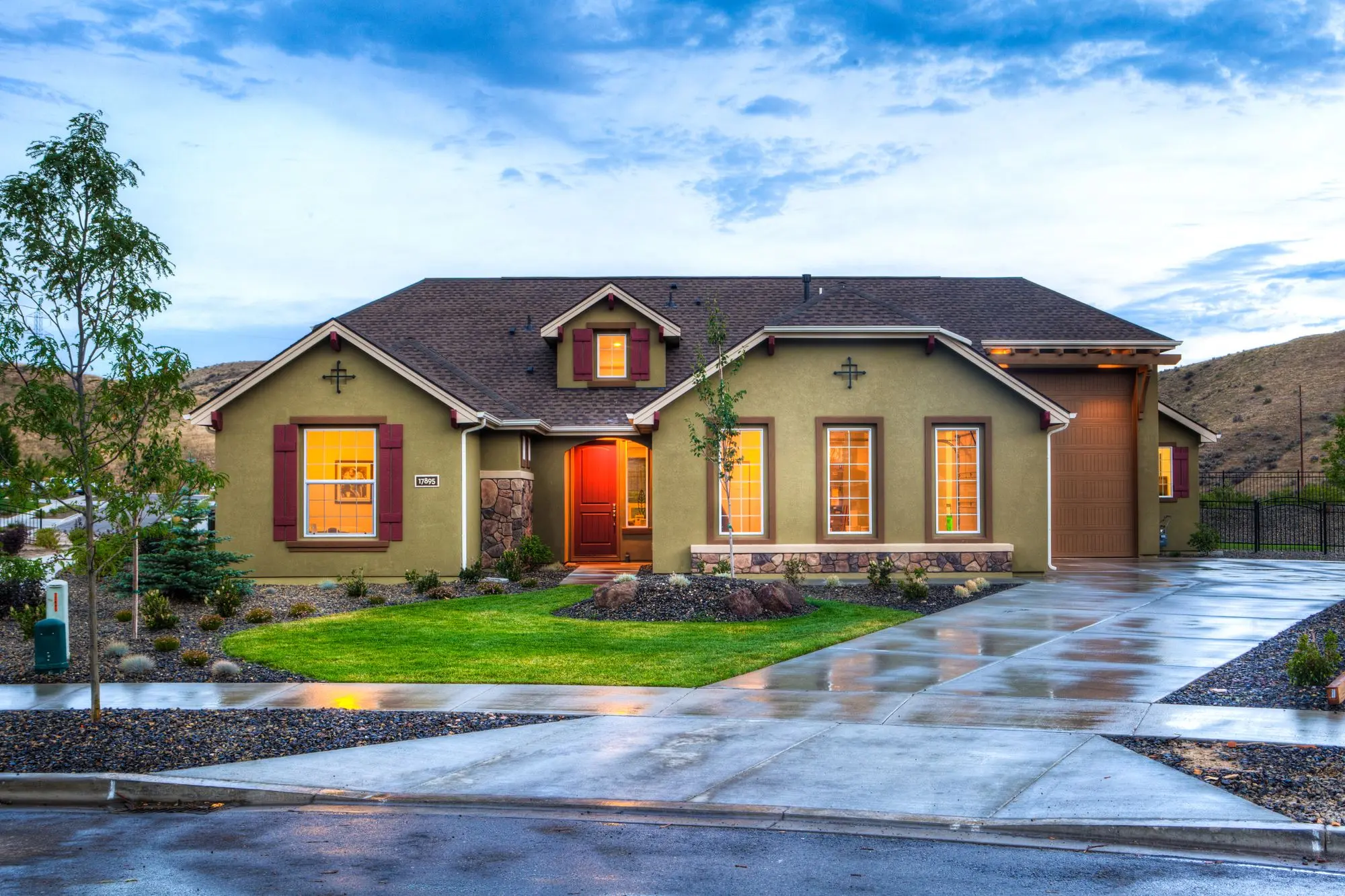 A modern house exterior lit at dusk, with a lawn and a wet driveway