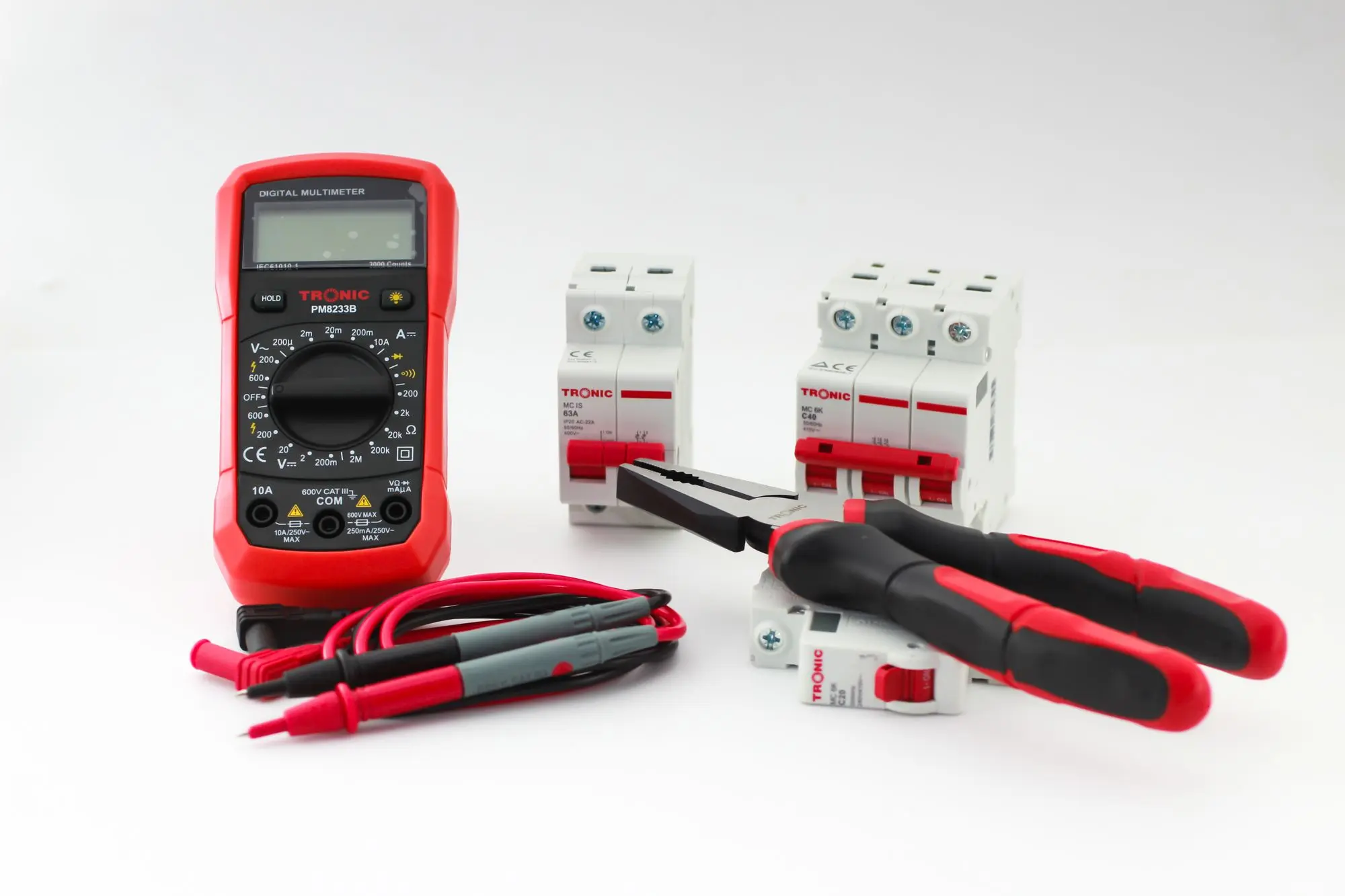 A digital multimeter lying beside hand tools and two circuit breakers on a white surface