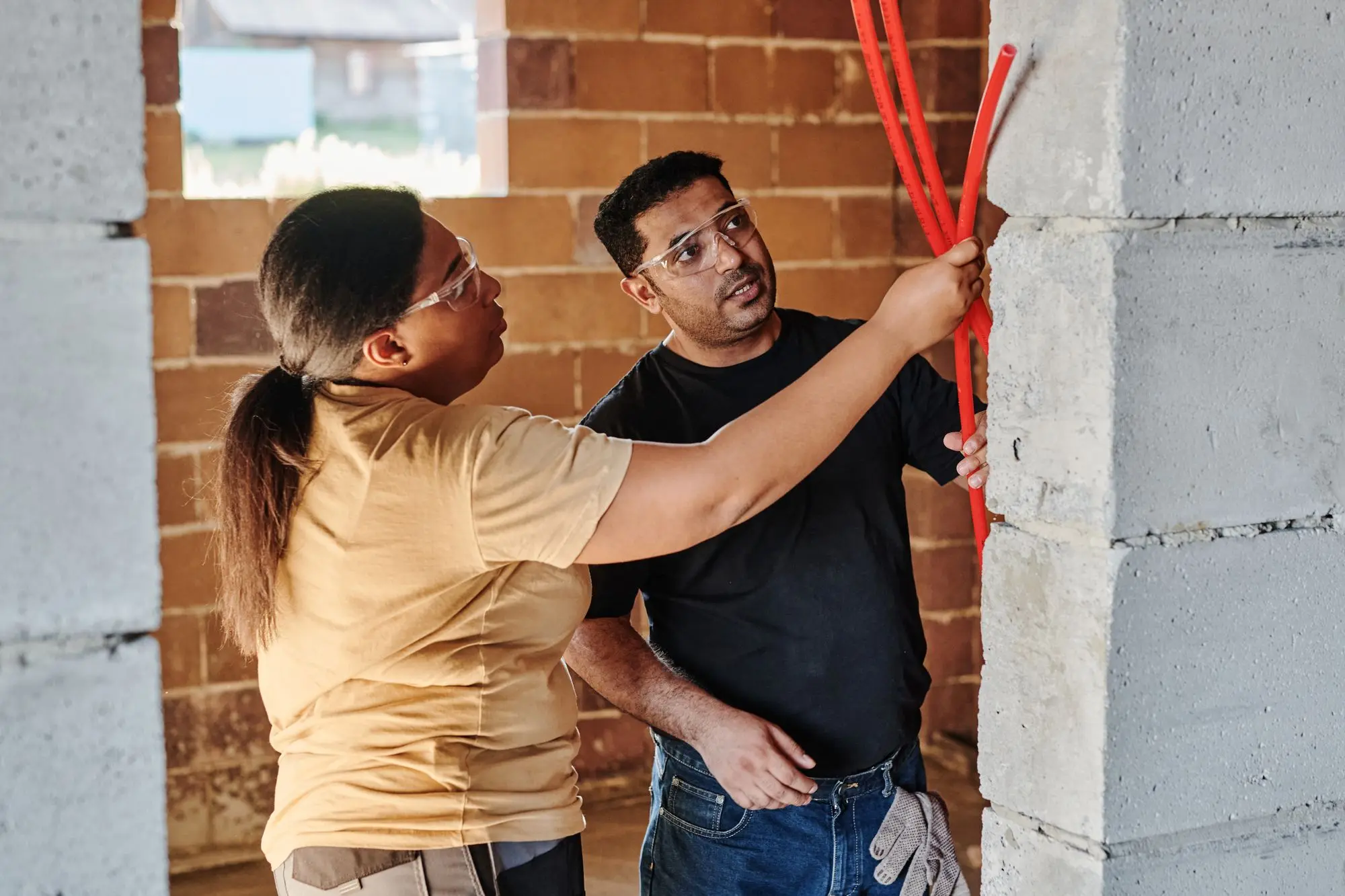 Two electricians assessing wiring inside an unfinished brick structure