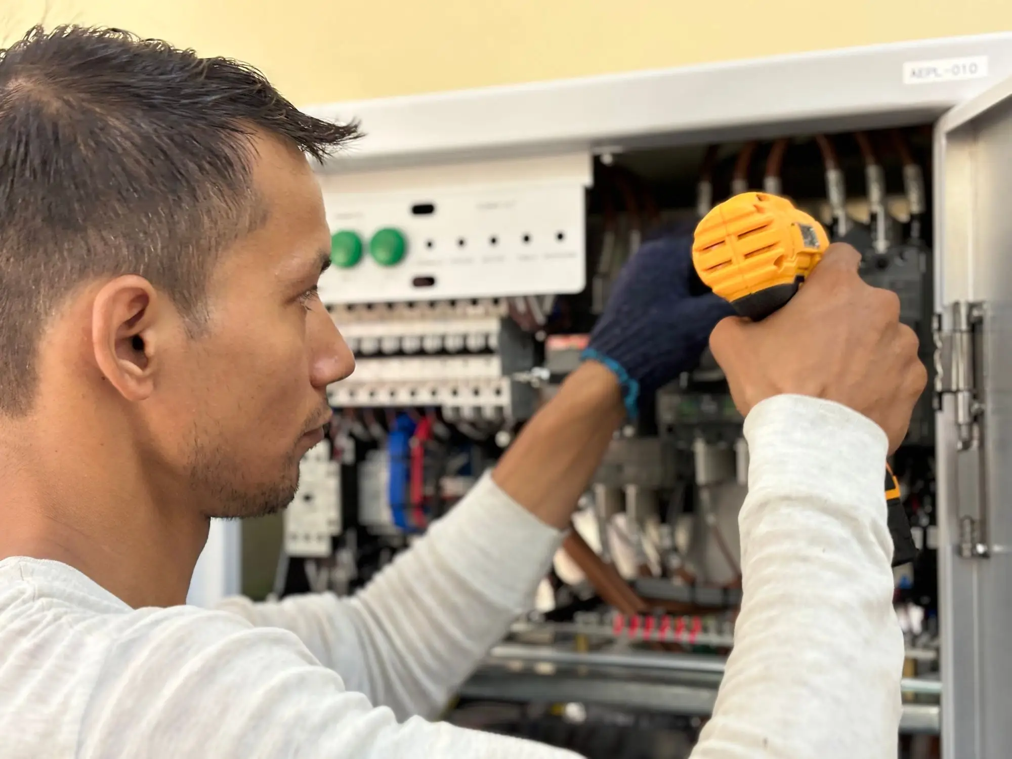 An electrician working on a panel with a cordless drill on site