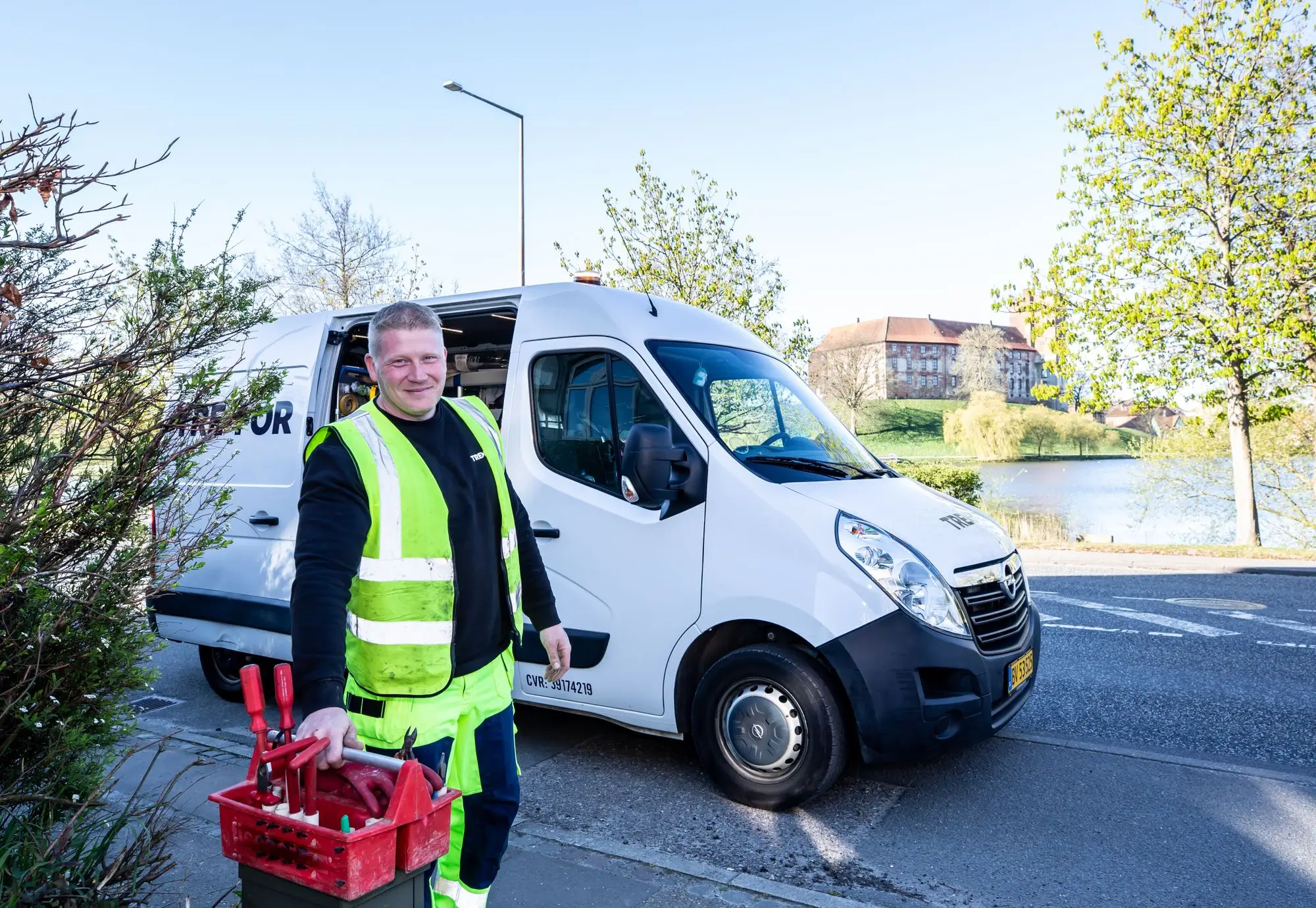 A worker in a high-visibility vest standing beside a work van holding tools